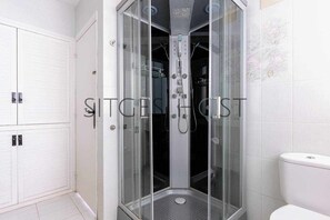 Une salle de bain moderne avec une douche à parois de verre, des murs recouverts de carreaux blancs et des toilettes.