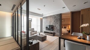 Et moderne hotelværelse med glasafskærmning, et fladskærms-tv, en seng, et skrivebord og et spiseområde.
