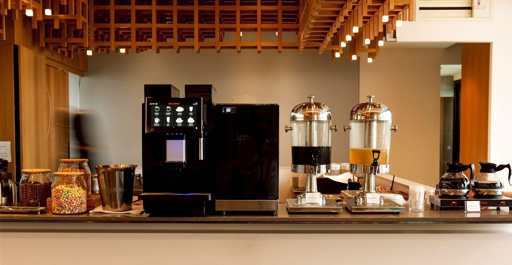 Eine Kaffeestation mit einer Kaffeemaschine, zwei Kaffeeautomaten und einer Auswahl an Gläsern mit verschiedenen Zutaten.