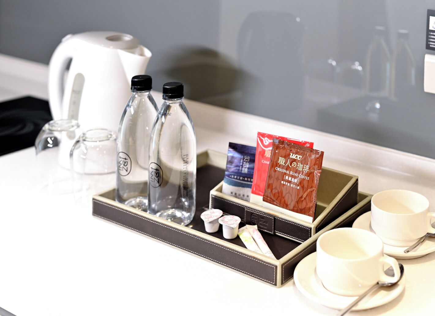 A hotel room's breakfast setup with a kettle, two water bottles, a tray with coffee packets, and tea bags.