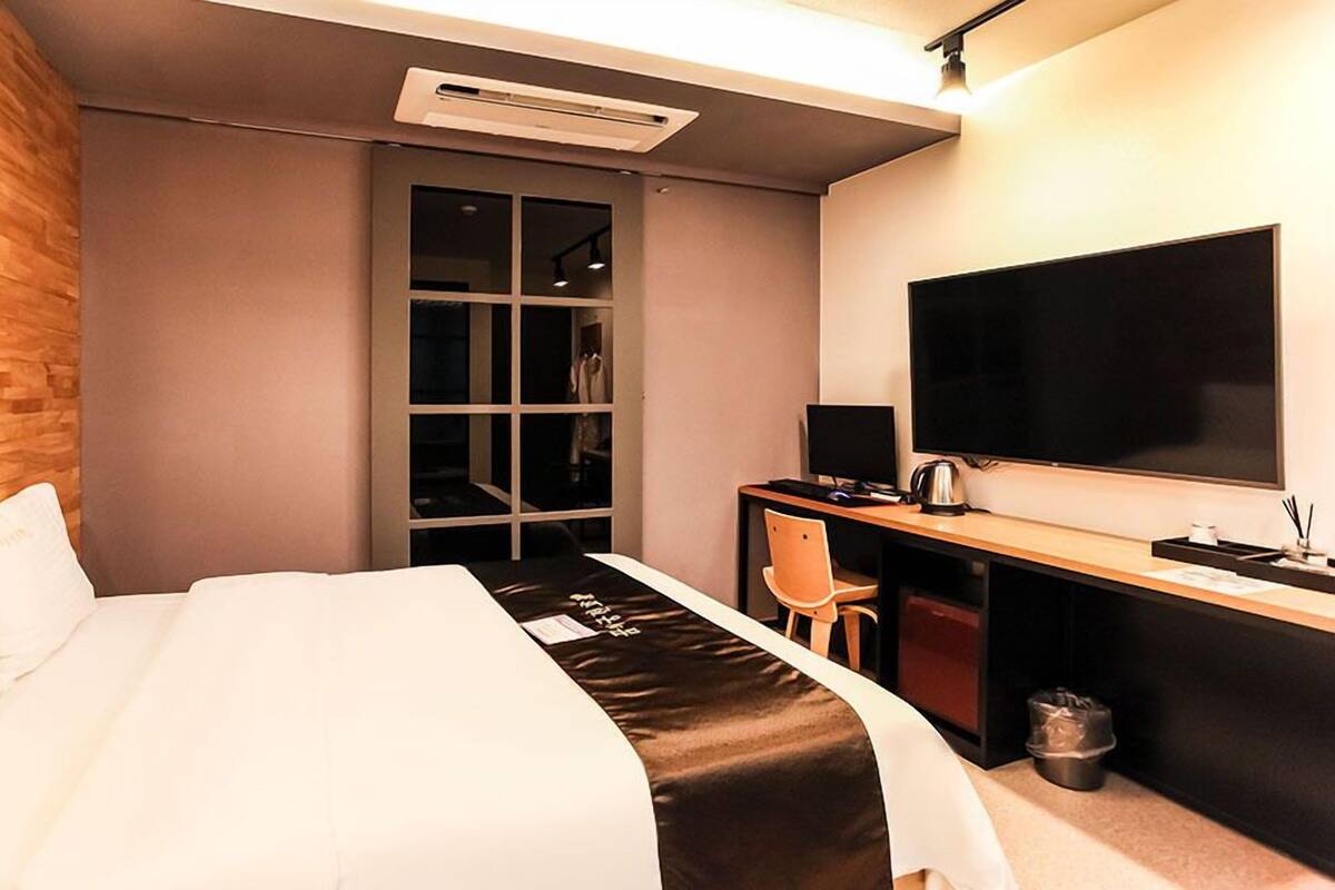 A hotel room with a bed, a desk with a computer, a TV, and a wardrobe.