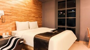Ein Hotelzimmer mit einem Holz-Kopfteil, einem Bett mit weißer Bettwäsche, einem schwarz-weiß gestreiften Sessel, einem Nachttischtelefon und einem Fenster mit Blick auf den Nachthimmel.