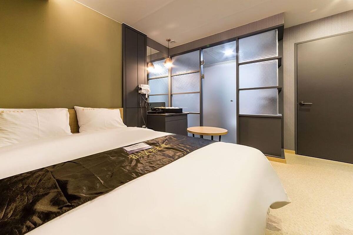 A modern hotel room with a large bed, a small round table, and a wardrobe with frosted glass doors.