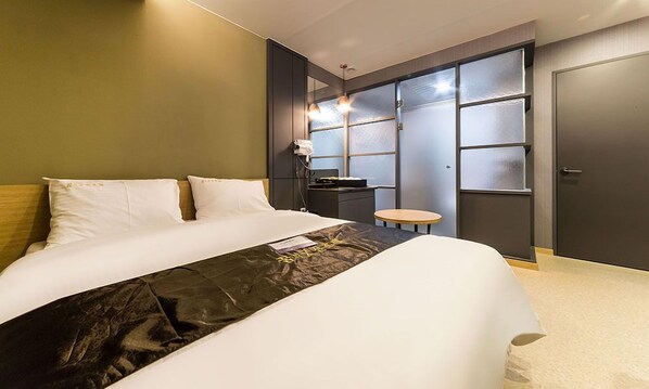 Une chambre d’hôtel moderne avec un grand lit, une petite table ronde et une armoire aux portes en verre dépoli.