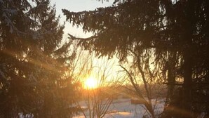 Un sendero cubierto de nieve que lleva a una valla de madera con un atardecer de fondo.