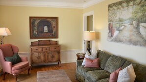 Una sala de estar con un mueble de madera, un sofá verde, un sillón rosa y un cuadro en la pared.