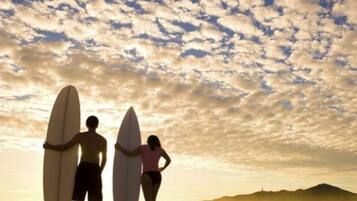 Two people holding surfboards on a beach with a cloudy sky.