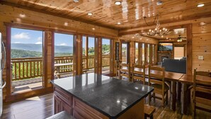 A wooden cabin interior with a kitchen area, dining space, and large windows offering mountain views. - Lookout Lodge ~ Indoor Pool, Hot Tub & Mountain Views! (Sevierville)