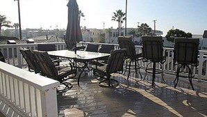 Une terrasse extérieure avec une table et des chaises, une balustrade blanche et des palmiers en arrière-plan.