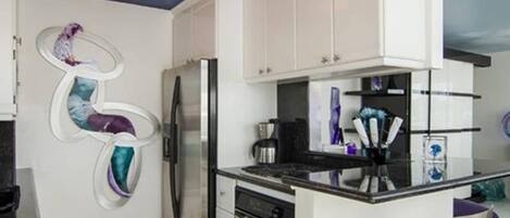 A modern kitchen with white cabinets, a stainless steel refrigerator, and a black countertop.