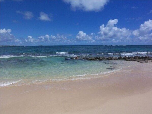 Enjoy the tranquil beach scene with clear waters and a natural breakwater.