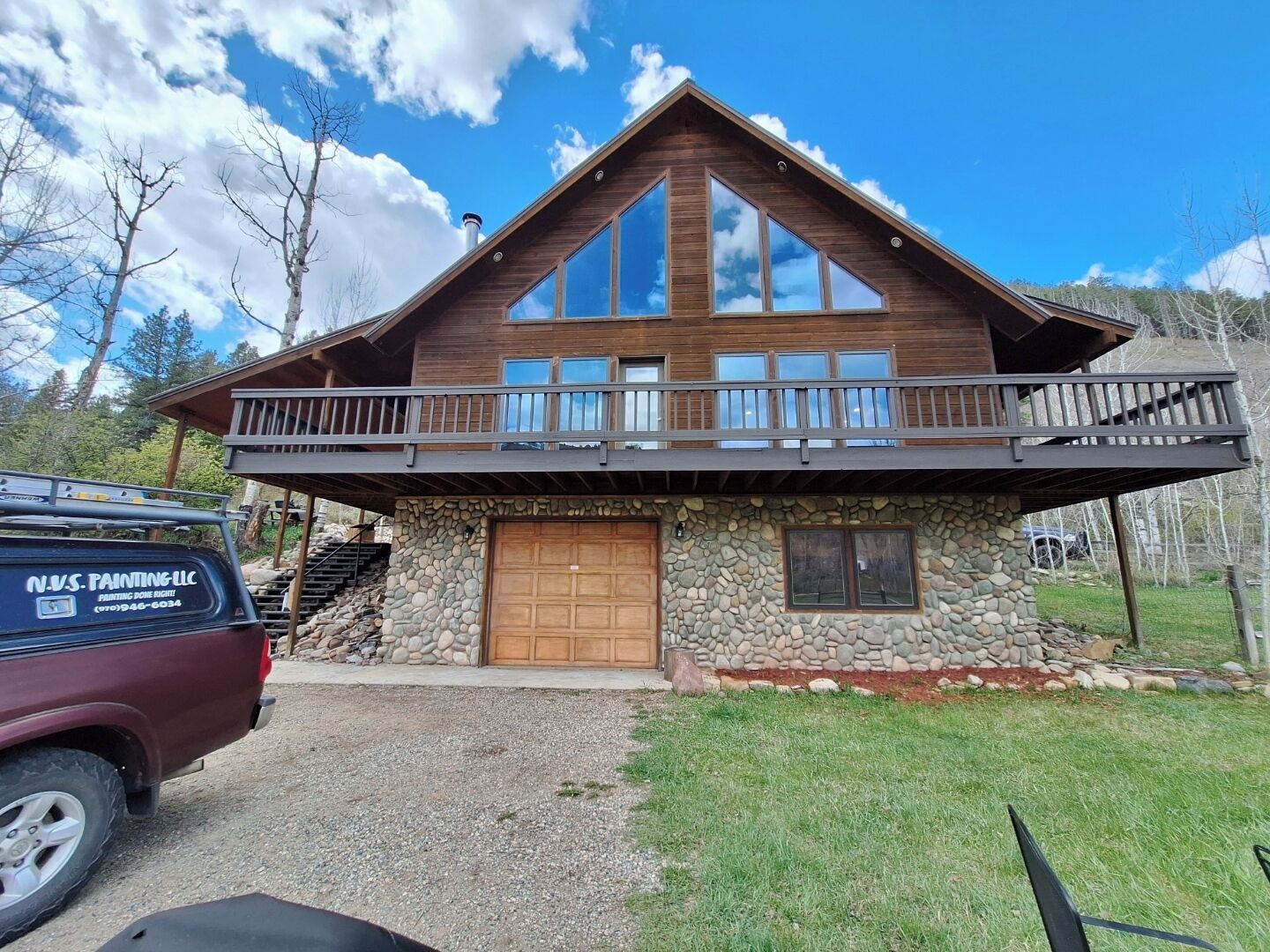 A two-story log cabin with a stone foundation, large windows, and a balcony.
