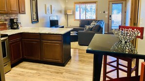 Una cocina moderna con armarios de madera oscura, encimera de mármol y estufa integrada. Hay una zona de comedor con una mesa de cristal y un cuenco decorativo.