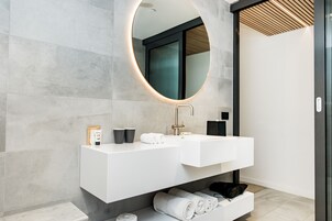 Un baño moderno con tocador blanco, un espejo redondo y un perchero para toallas.