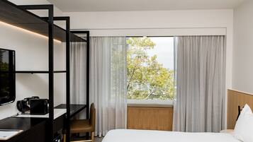 Habitación de hotel con cama, escritorio, silla, televisión y ventana con cortinas.