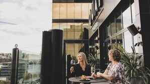 An outdoor dining area with a view of a modern building and a glass railing. - Quay Perth (Perth)
