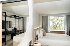 Quarto de hotel moderno com uma cama, uma escrivaninha e uma janela grande com cortinas.