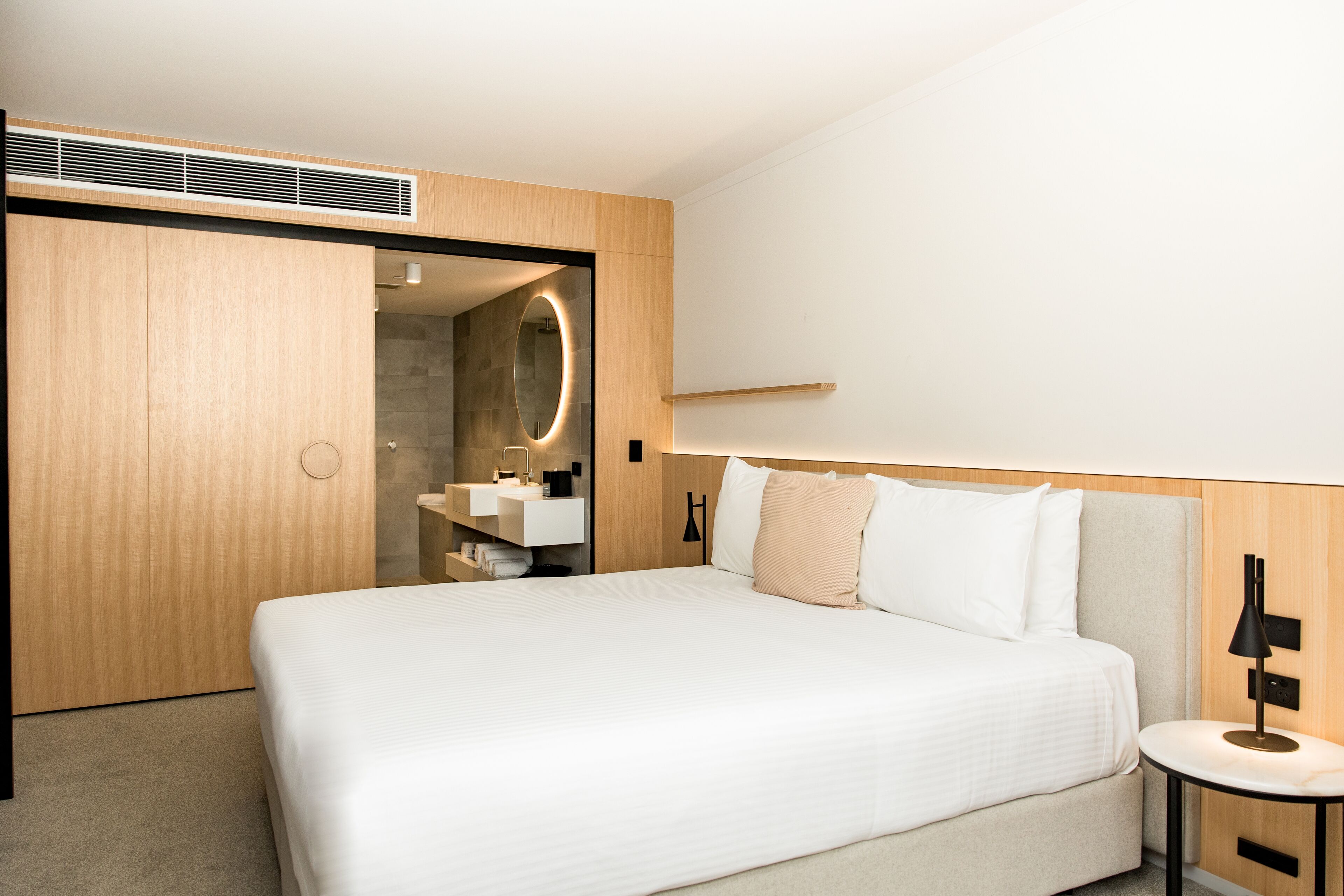 Una habitación de hotel moderna con una cama grande, una mesita de noche, un espejo y un armario empotrado.