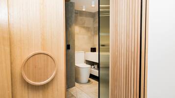 Un baño moderno con puerta de madera, inodoro y mampara de vidrio.