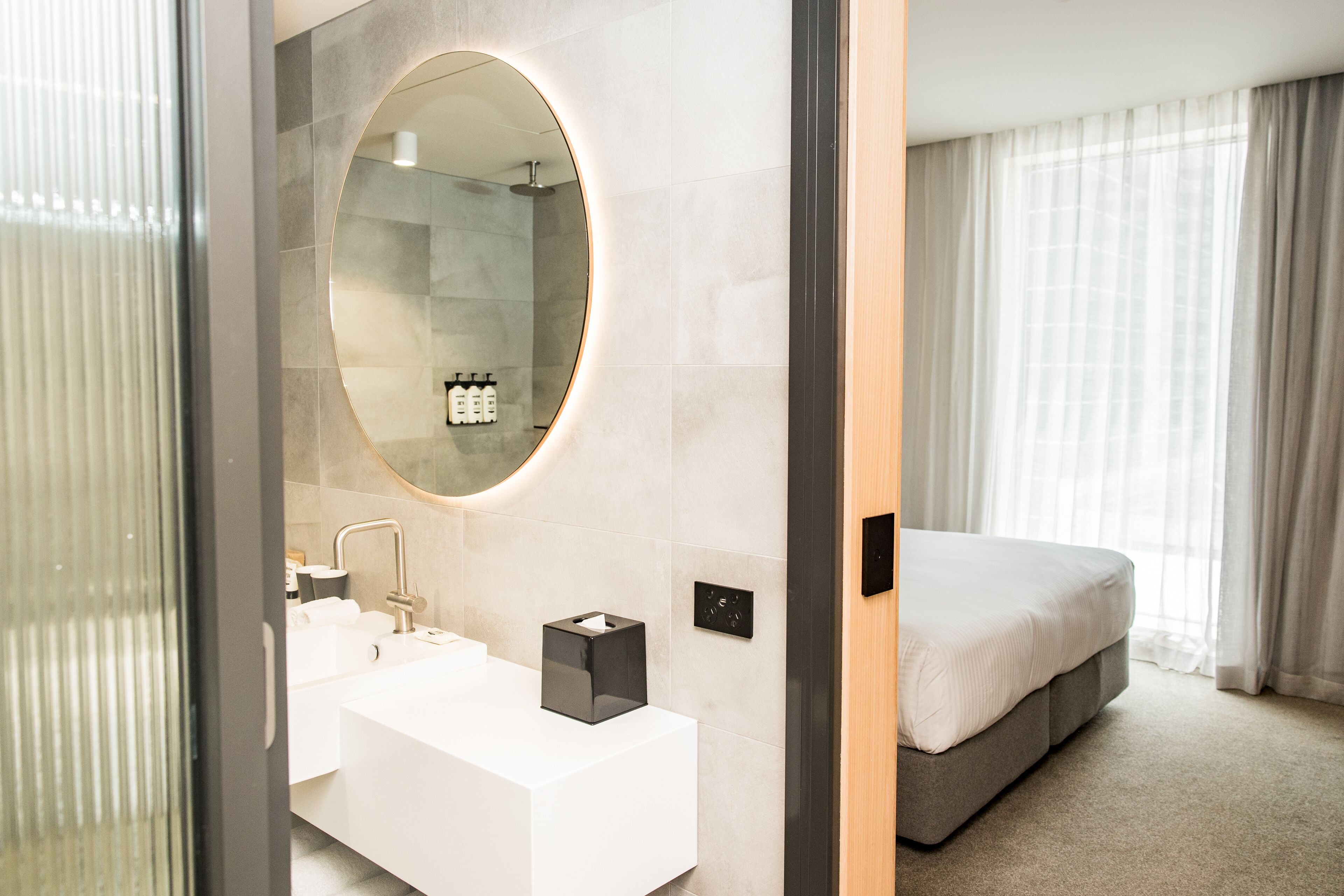 Uma casa de banho moderna com um espelho grande, lavatório branco e uma mesa de cabeceira com caixa de lenços.