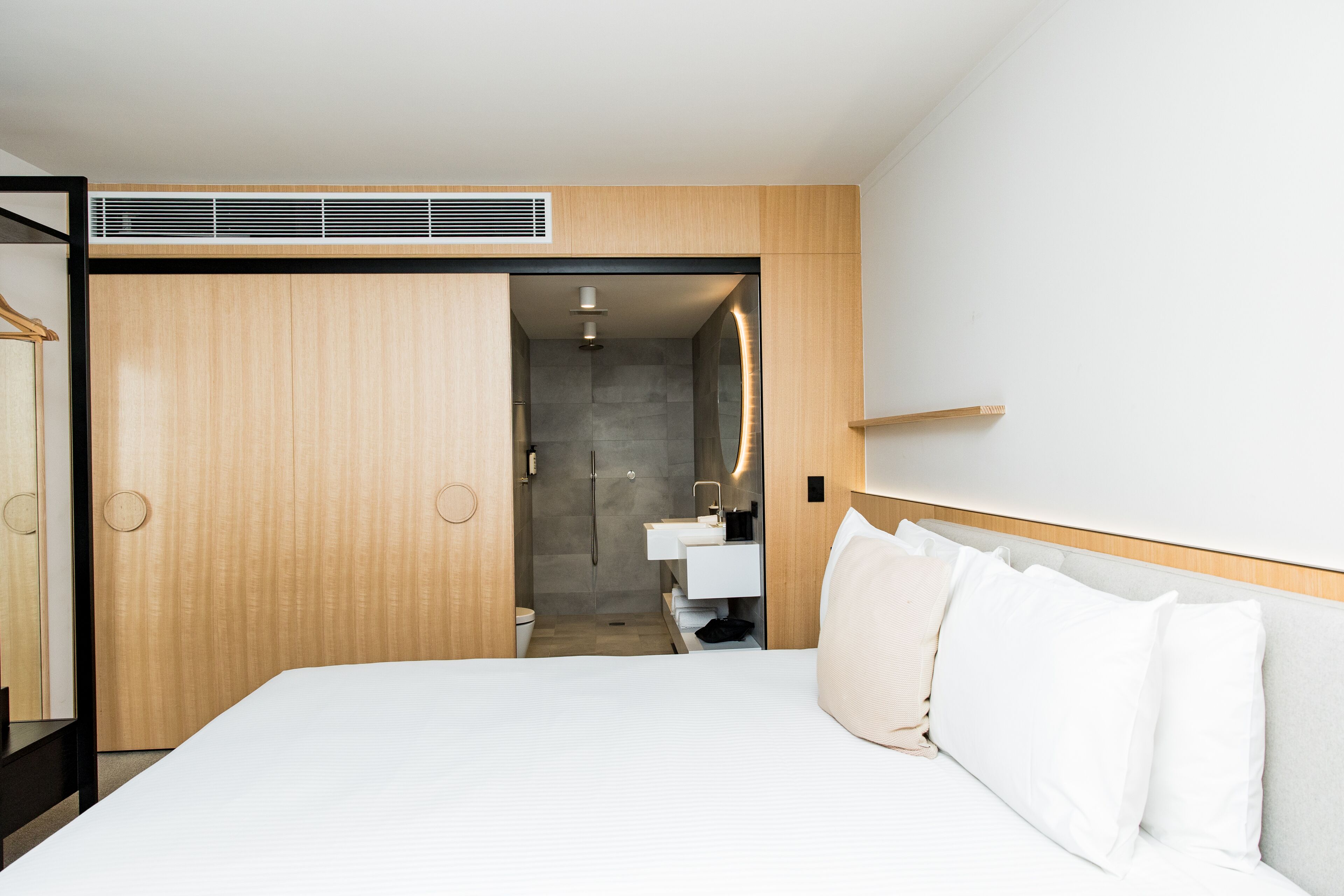 A hotel room with a bed, a wooden wardrobe, a bathroom with a sink, and a shower.
