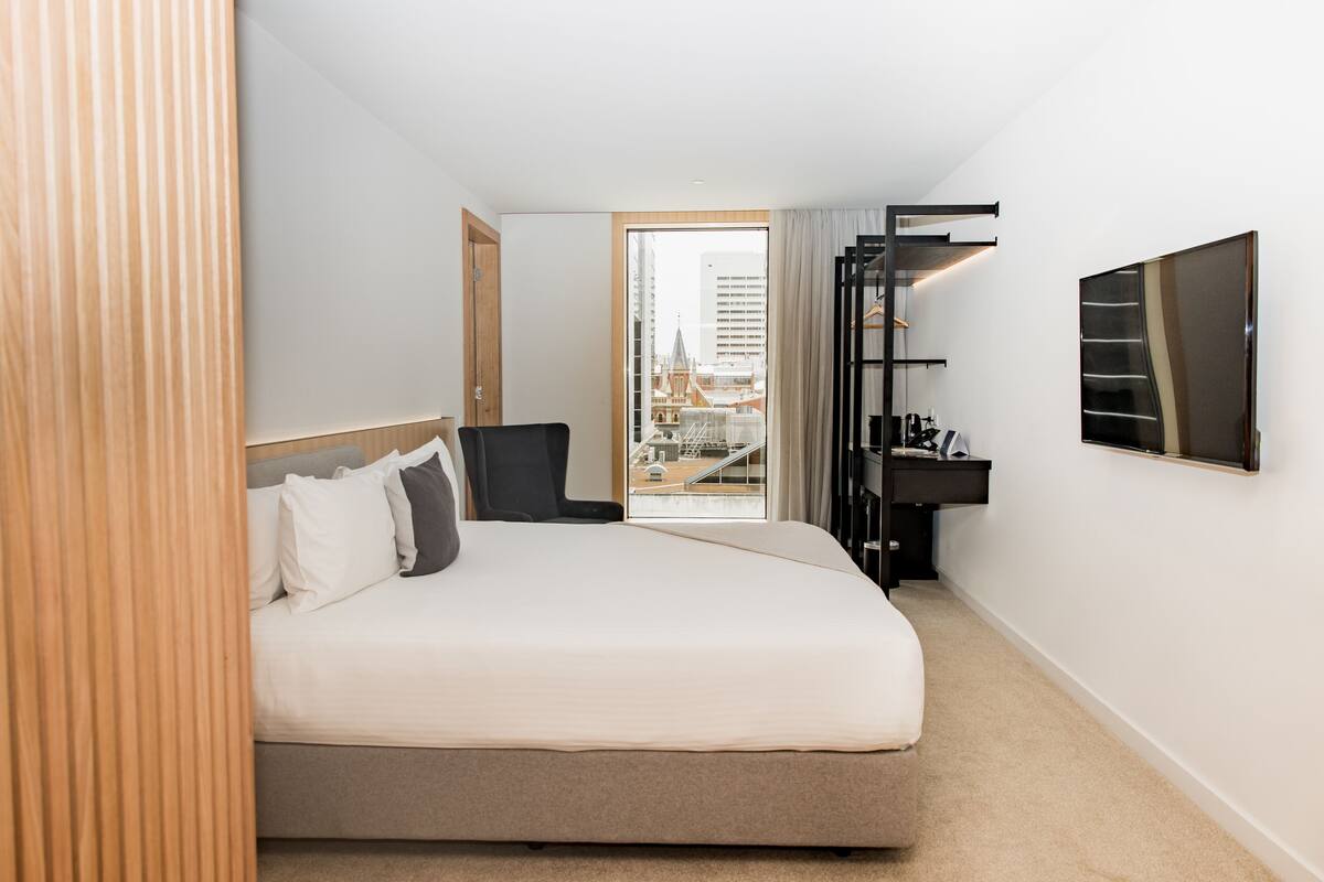 Une chambre d’hôtel équipée d’un lit, d’un bureau, d’une chaise, d’une télévision et offrant une vue sur le paysage urbain.