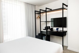 Una camera d'albergo moderna con un letto, una scrivania con TV a schermo piatto e un armadio con attaccapanni.