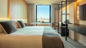 A hotel room with a large bed, a desk with a TV, a balcony with a city view, and a window with curtains. - Quay Perth (Perth)