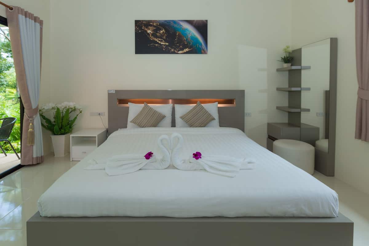 Een netjes opgemaakt bed met handdoeken gevouwen in de vorm van zwanen, een nachtkastje, een kamerplant en een wanddecoratie.