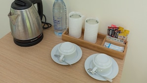 Une table avec une bouilloire, une bouteille d’eau, deux rouleaux de papier toilette, un plateau avec des sachets de café et deux tasses avec leurs soucoupes.