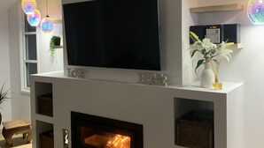 A modern living room with a large flat-screen TV, a fireplace, and decorative lighting.