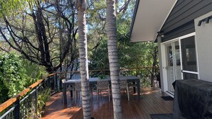 A wooden deck with a table and chairs, surrounded by trees and a house.