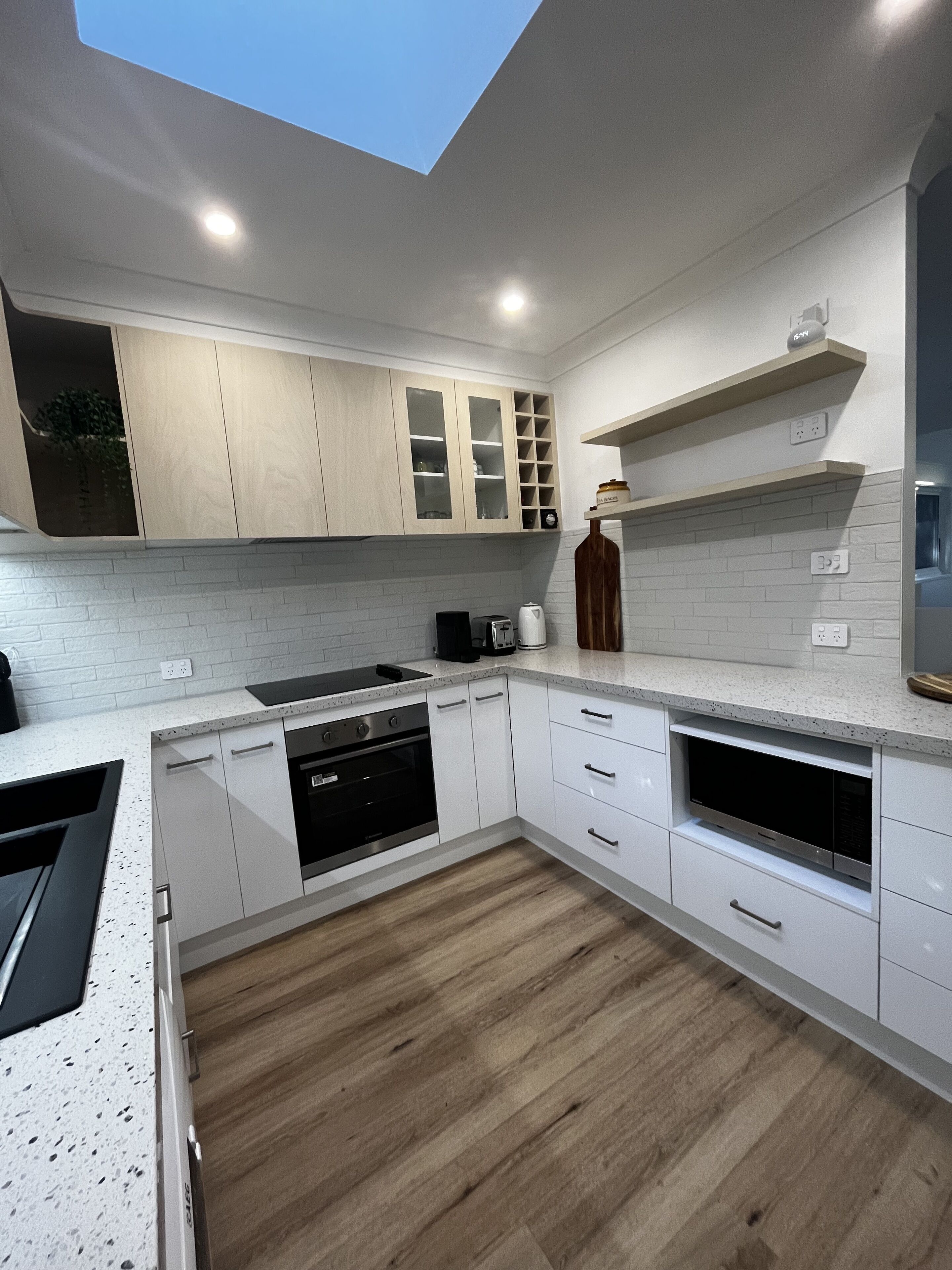 A modern kitchen with white cabinetry, a wooden floor, and built-in appliances.