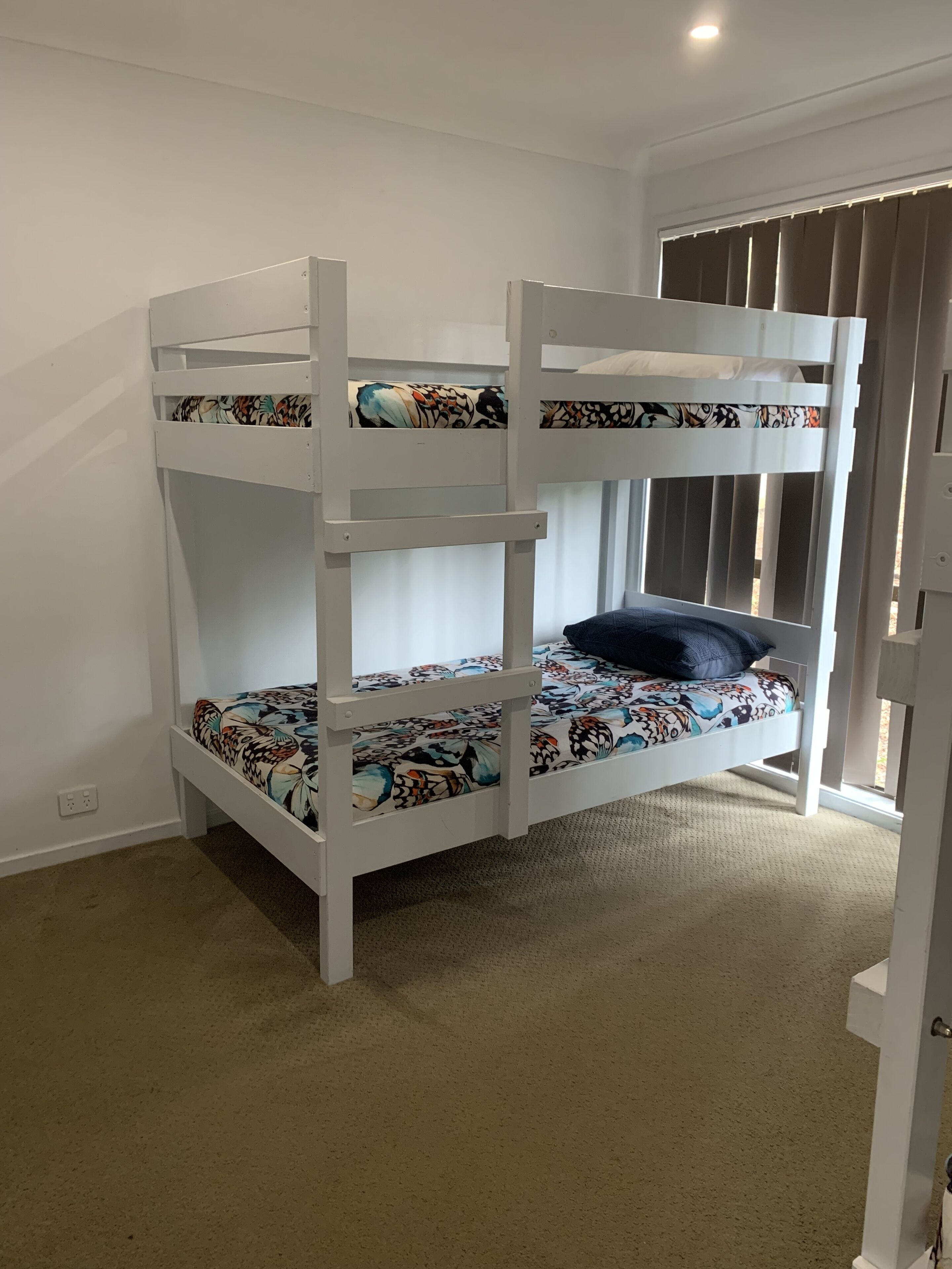 A bunk bed with patterned bedding, a window with blinds, and a carpeted floor.