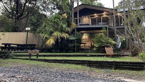 A two-story building with a balcony, surrounded by tropical vegetation.