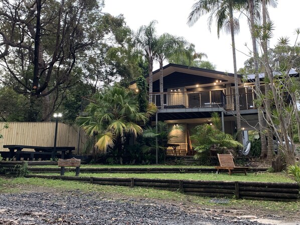 A two-story building with a balcony, surrounded by tropical vegetation. - Family Friendly Beach House - 2min walk to Beach, Bushwalks & Open Fireplace (Vincentia)