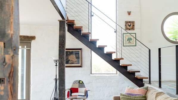 Un escalier avec des marches en bois et une rampe en métal, un tableau encadré au mur, une lampe et une chaise avec un coussin coloré.