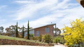 Una casa moderna con techo inclinado, rodeada por un muro de piedra y diversas plantas.