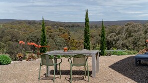 Un espace extérieur aménagé avec une table et deux chaises, entouré d’un chemin de gravier et de différentes plantes.