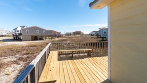 Una terraza de madera con un banco, con vista a una playa y casas al fondo.