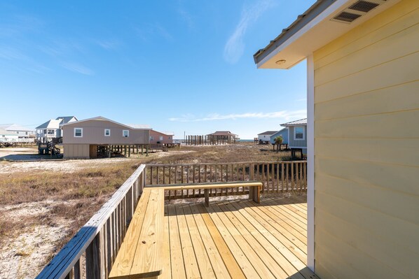A wooden deck with a bench, overlooking a beach with houses in the background.