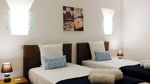 Hotellihuoneessa on kaksi sänkyä, joissa on valkoiset lakanat ja kuviolliset tyynyt. Seinälle on asennettu lamput, ja sänkyjen yläpuolella on kehystetty taulu.