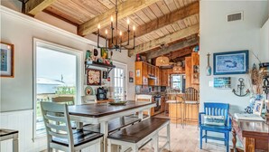 A rustic kitchen with wooden beams, a dining area with white chairs, and a blue chair with a 'Sail Away' pillow. - Sea Dog- Pool, Crows Nest, Great View! 3 Bedrm,/3 Bath, Pet Friendly, Sleep 11 (Dauphin Island)