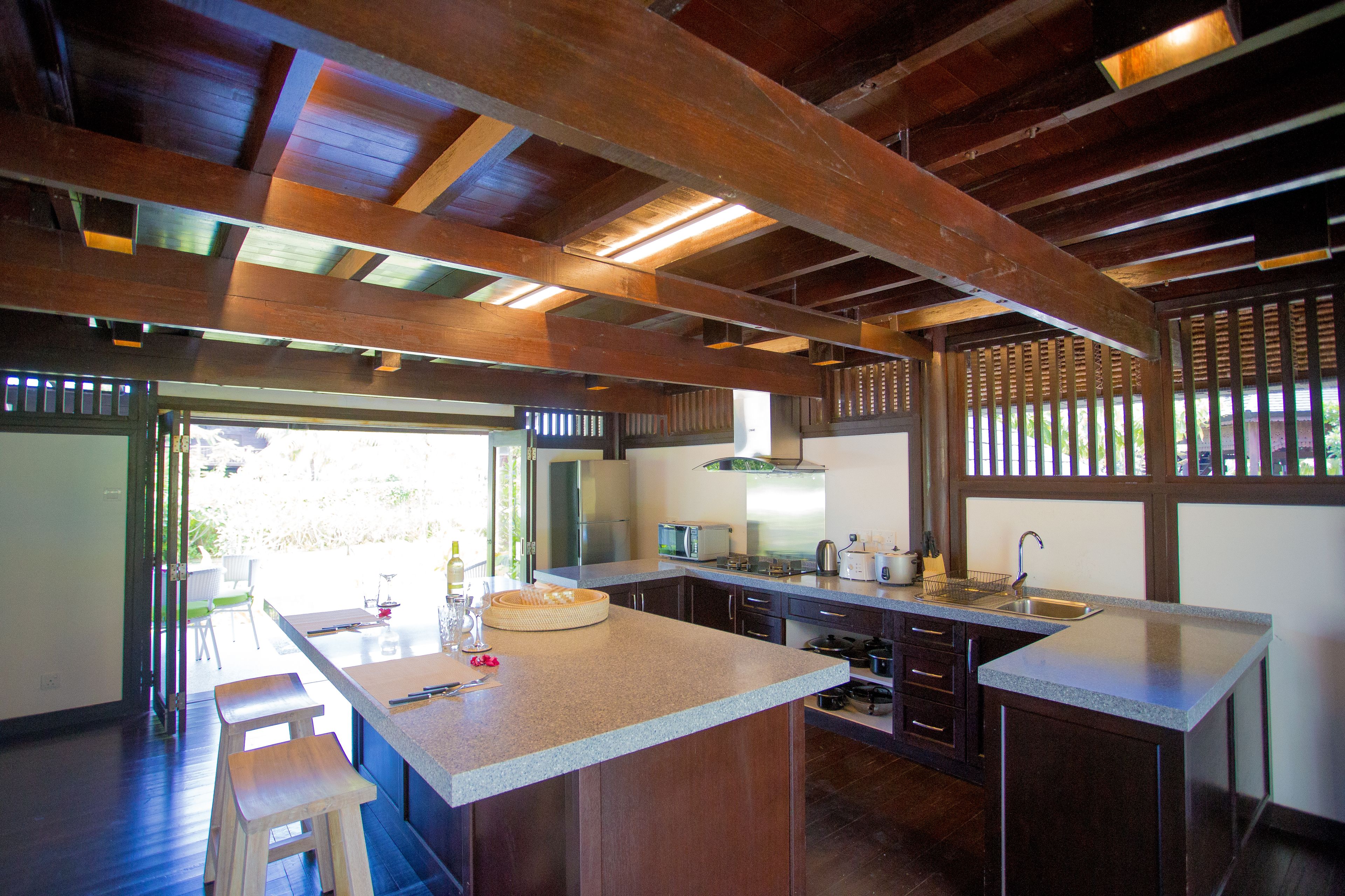 A modern kitchen with wooden beams, a large island, and a view to the outside.