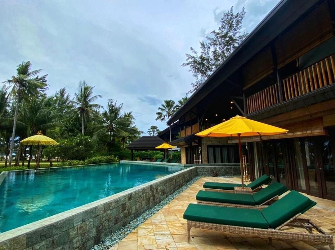 A swimming pool with lounge chairs and umbrellas, surrounded by palm trees and a building with a balcony.