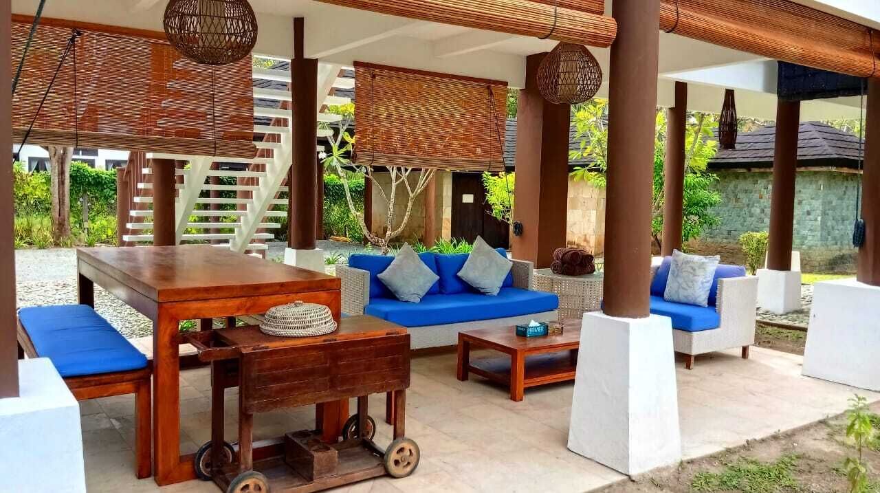 A covered outdoor seating area with a wooden table, blue sofa, and white chairs.