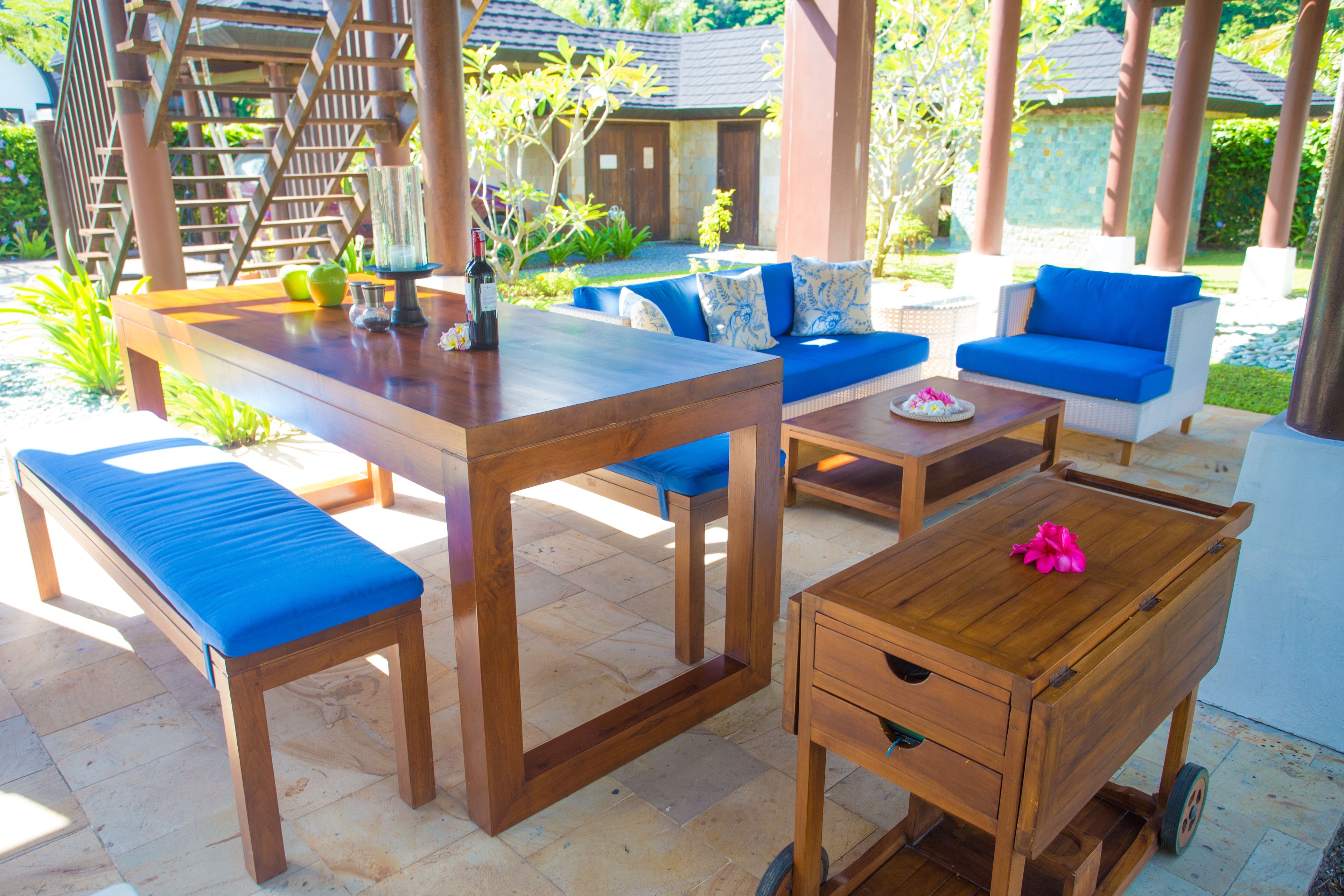 A wooden outdoor seating area with benches and a table, surrounded by greenery and a wooden pergola.