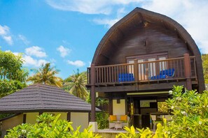 A wooden villa with a balcony, surrounded by lush greenery.