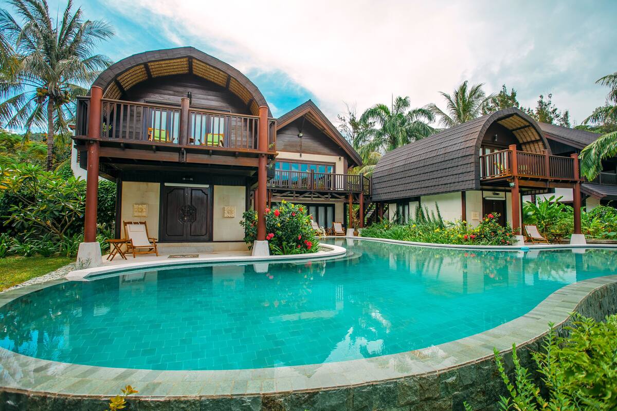 A resort with a large swimming pool, wooden balconies, and lush tropical vegetation.