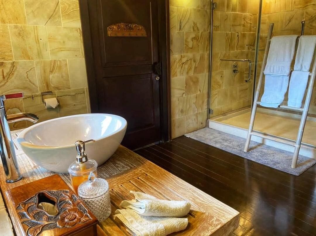 A bathroom with a large white sink, a wooden vanity, a glass jar, and a towel rack with towels.